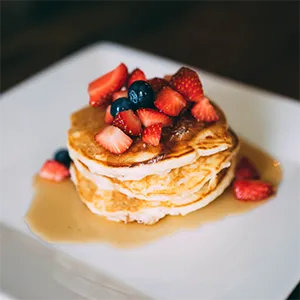 A photo of a stack of pancakes with fresh fruit and syrup